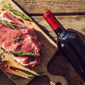 Raw pork steak with bottle of red wine, meat fork and rosemary o